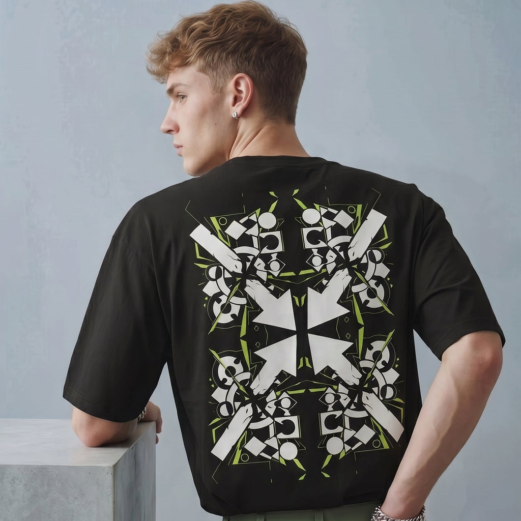 Person wearing a black t-shirt with a white and green pattern on the back, standing against a gray background.
