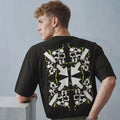 Person wearing a black t-shirt with a white and green pattern on the back, standing against a gray background.